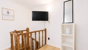 Ein Zimmer mit einer Holztreppe, einem an der Wand befestigten Flachbildfernseher und einem weißen Regalschrank.