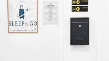 A wall with a framed sign reading 'SLEEP & GO,' a small window, and a black intercom system with directional signs.