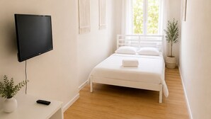 Ein Schlafzimmer mit einem Bett, einem Fernseher, einem Regal mit einer Pflanze und einem Fenster.