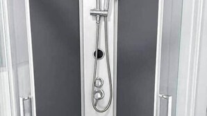 Eine Eckdusche mit Glastür, Handbrause und Ablauf in der Bodenfläche.