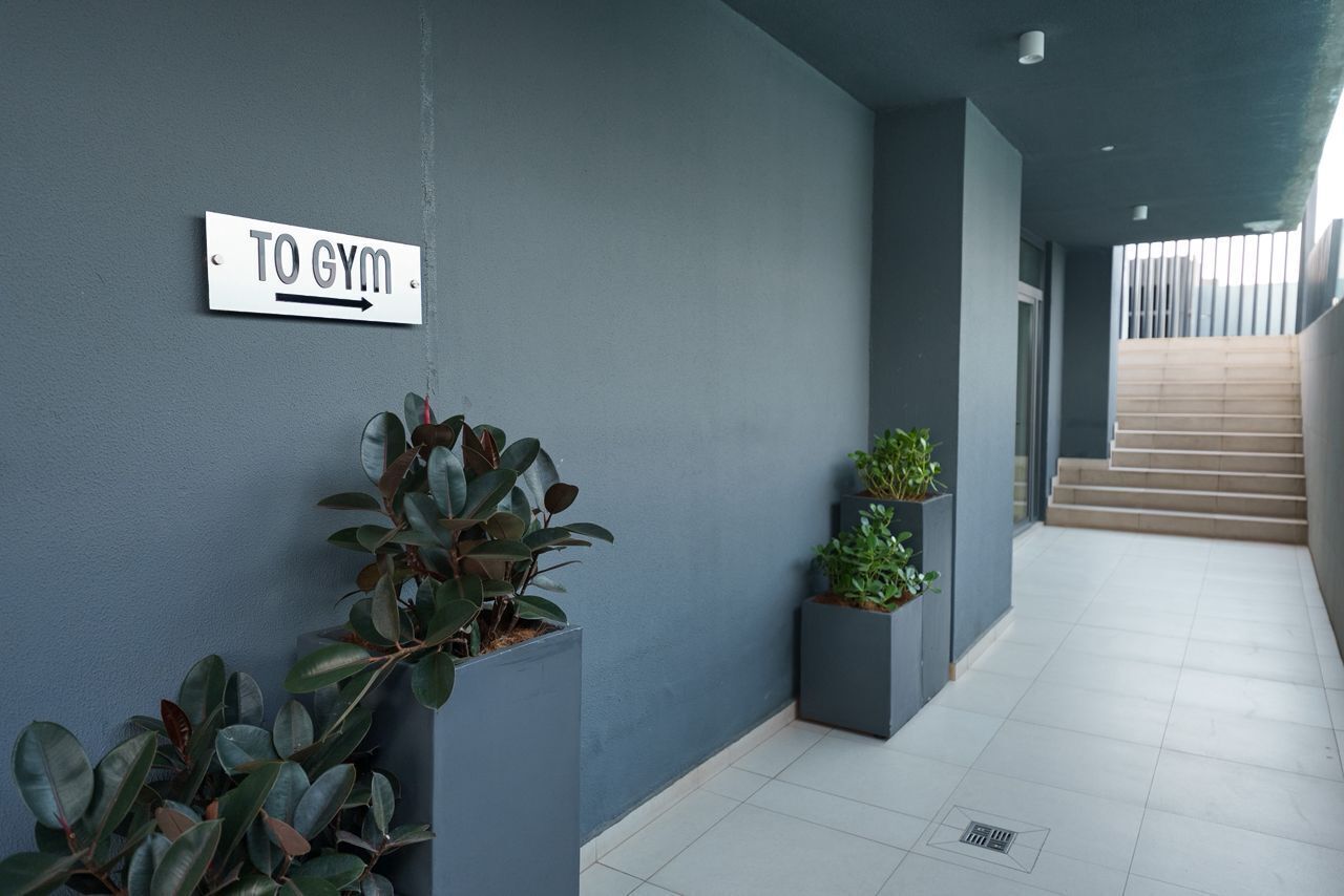 A hallway with a sign pointing to the gym, potted plants, and a staircase.