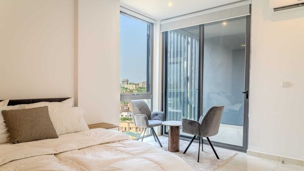 Een slaapkamer met een bed, een stoel, een klein tafeltje en een grote glazen schuifdeur die leidt naar een buitenbalkon.