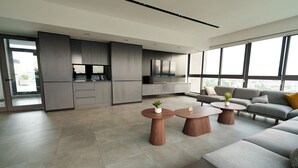 Een moderne woonkamer met een bank, twee salontafels en een keukenhoek met kastjes en een televisie.