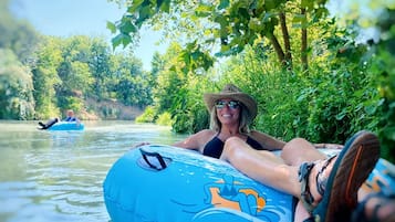 Una persona recostada sobre una balsa inflable azul en un río rodeado de follaje.