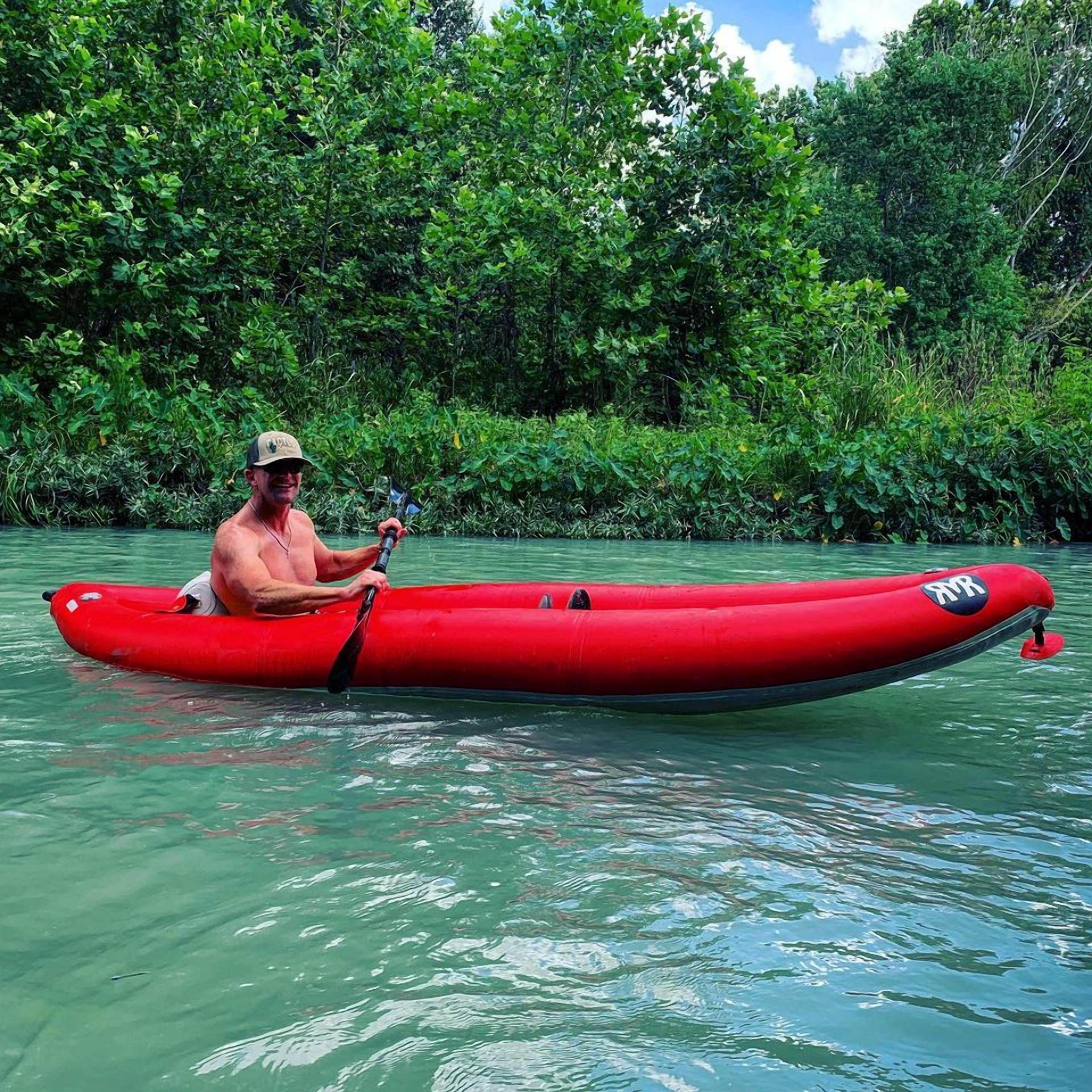 A person in a red kayak on a calm body of water surrounded by dense green foliage.