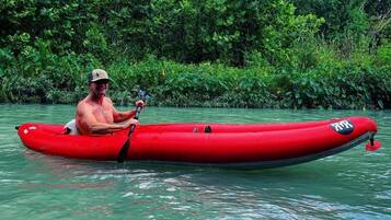 A person in a red kayak on a calm body of water surrounded by dense green foliage.