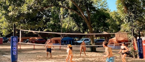 A beach volleyball game with tents and cars in the background.