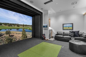 Un salon moderne avec une grande fenêtre, un canapé en cuir, une télécommande et un sac de golf.