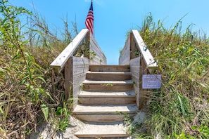 A wooden staircase leading up to a beach entrance with an American flag, surrounded by tall grasses and a sign indicating private property. - Sea Breeze enjoy oceanviews and a charming 3-bedroom retreat in Surf City. (Surf City)
