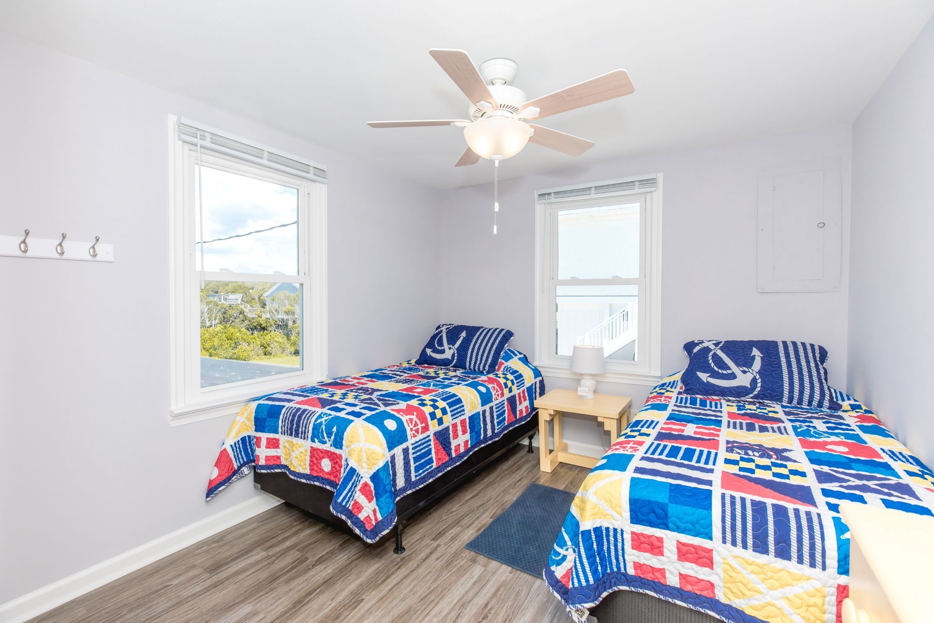 A bedroom with two beds, a ceiling fan, and large windows.