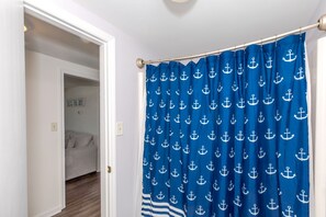 Une pièce avec un rideau bleu orné de motifs d’ancres blancs, un lit et un panneau accroché au mur sur lequel on peut lire : « PROFITEZ DE CHAQUE INSTANT ».