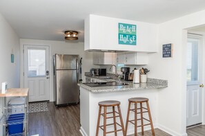 A modern kitchen with a stainless steel refrigerator, a microwave, and a coffee maker. There are two wooden stools and a sign that reads 'Beach House.' - Sea Breeze enjoy oceanviews and a charming 3-bedroom retreat in Surf City. (Surf City)