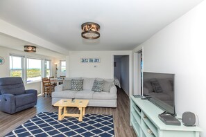 A modern living room with a sofa, a television, and a dining area with a table and chairs. - Sea Breeze enjoy oceanviews and a charming 3-bedroom retreat in Surf City. (Surf City)