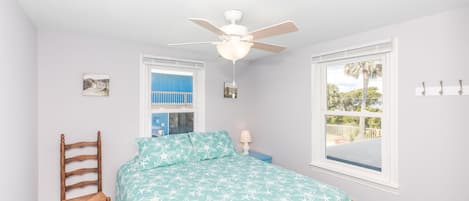 A bedroom with a bed, a ceiling fan, a window with a view, and a chair.