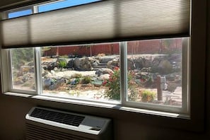Une fenêtre donnant sur un jardin, un store et une bouche d’aération fixée au mur.
