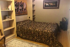 Ein Schlafzimmer mit einem gemusterten Bettüberwurf, einem Teppich, einem Regal mit Dekorationen und einem Bild an der Wand.