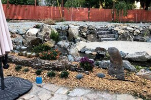 Ein Garten mit einer Steinskulptur, einem roten Zaun und einer Steinmauer.