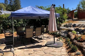 A patio area with a stone table and chairs, a tent, and an umbrella.