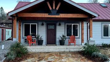 A house with a red roof, a wooden porch, two potted plants, and a gravel driveway.