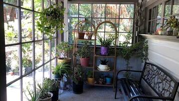 A covered patio area with a metal bench, potted plants, and a window with a view of greenery.