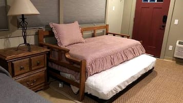 Een slaapkamer met een houten bed, nachtkastje, lamp, raam met zonwering en een deur.