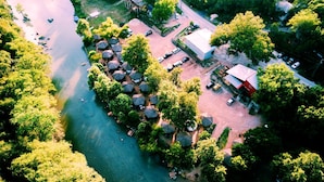 Luchtbeeld van een pand aan de rivier met een groep rieten hutten, een hoofdgebouw en een parkeerplaats.