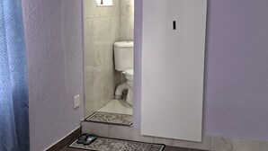 Casa de banho com sanita, zona de duche e porta para outro espaço.
