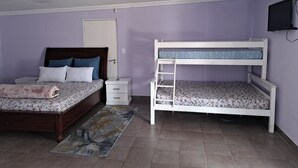 Quarto com cama de madeira, beliche, mesa de cabeceira, cômoda e televisão fixada na parede.