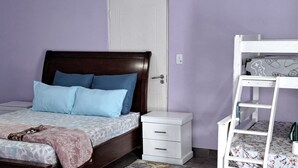 Quarto com cama de madeira, mesa de cabeceira branca, penteadeira branca e beliche.