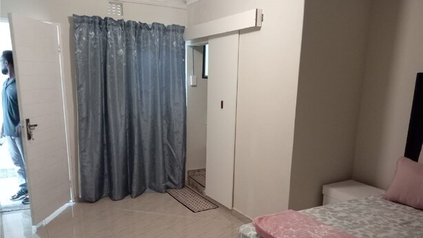 Quarto com cama, banheiro com cortina de chuveiro e porta para outro cômodo.