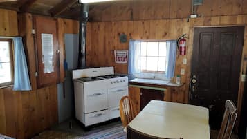 A wooden cabin interior with a stove, a table, and a chair.