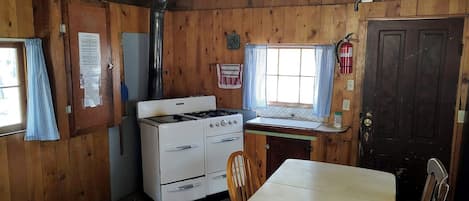 A wooden cabin interior with a stove, a table, and a chair.