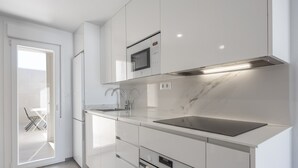 Una cuina moderna amb armaris blancs, microones integrat, vàter d'acer inoxidable i frontissa de marbre.