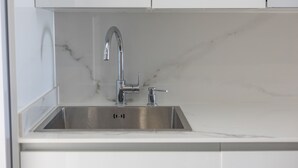 Una cuina moderna amb un vàter d'acer inoxidable, armaris blancs i una posterior d'marbre.