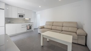 Una cuina moderna amb armaris blancs, un microones i un sofà beix a la zona d'estar.