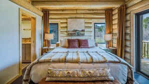 Ein Schlafzimmer in einer Blockhütte mit einem Bett, zwei Nachttischen, einem Schreibtisch und einem Fenster, sowie einer Tür zu einem anderen Raum.
