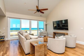 A spacious living room with a large window, a ceiling fan, a flat-screen TV, and a fireplace. - Seascape - 4BR, Oceanfront, Dog Friendly, Fully Renovated! (Topsail Beach)