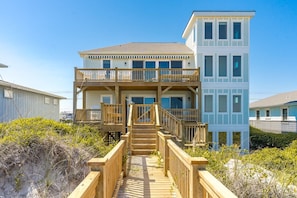 A two-story beachfront house with a wooden deck leading to a balcony, surrounded by vegetation. - Seascape - 4BR, Oceanfront, Dog Friendly, Fully Renovated! (Topsail Beach)