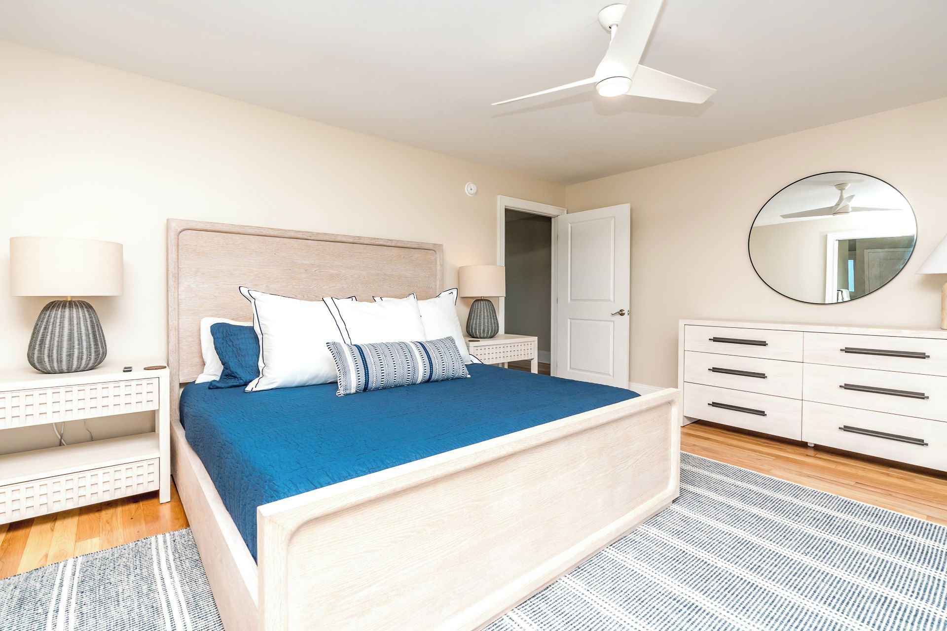 A bedroom with a bed, bedside tables, a dresser, a ceiling fan, and a mirror.
