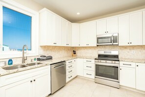 A modern kitchen with white cabinets, stainless steel appliances, and a view of the ocean through a window. - Seascape - 4BR, Oceanfront, Dog Friendly, Fully Renovated! (Topsail Beach)