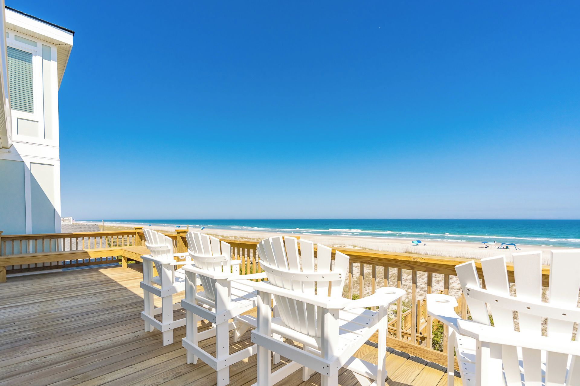 A deck with white chairs and tables overlooking a beach.