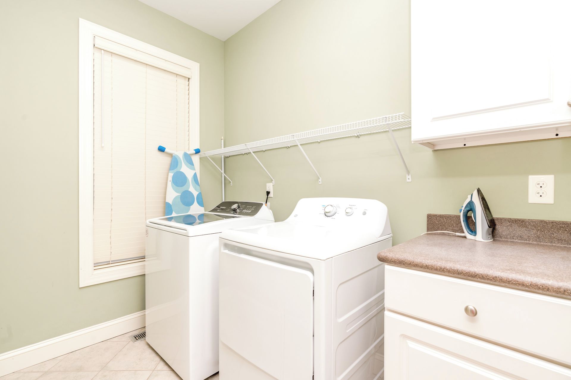 A laundry room with two white washing machines, a drying rack, and an ironing board.