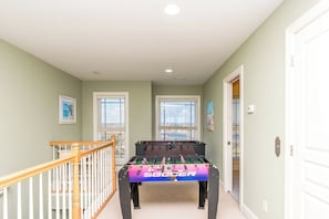 A hallway with a foosball table, a staircase, and two windows with blinds. - Sea Escape - Incredible Oceanfront 8 BR Home in Gated Community (North Topsail Beach)