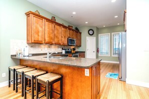 A kitchen with wooden cabinets, a granite countertop, a microwave, and a refrigerator. - Sea Escape - Incredible Oceanfront 8 BR Home in Gated Community (North Topsail Beach)