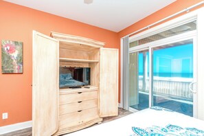 A room with an open wooden wardrobe, a bed with a patterned bedspread, and a view of the ocean through a sliding glass door. - Sea Escape - Incredible Oceanfront 8 BR Home in Gated Community (North Topsail Beach)