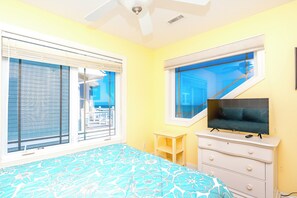 A bedroom with a bed, a TV, a dresser, and a window with a view of a balcony. - Sea Escape - Incredible Oceanfront 8 BR Home in Gated Community (North Topsail Beach)