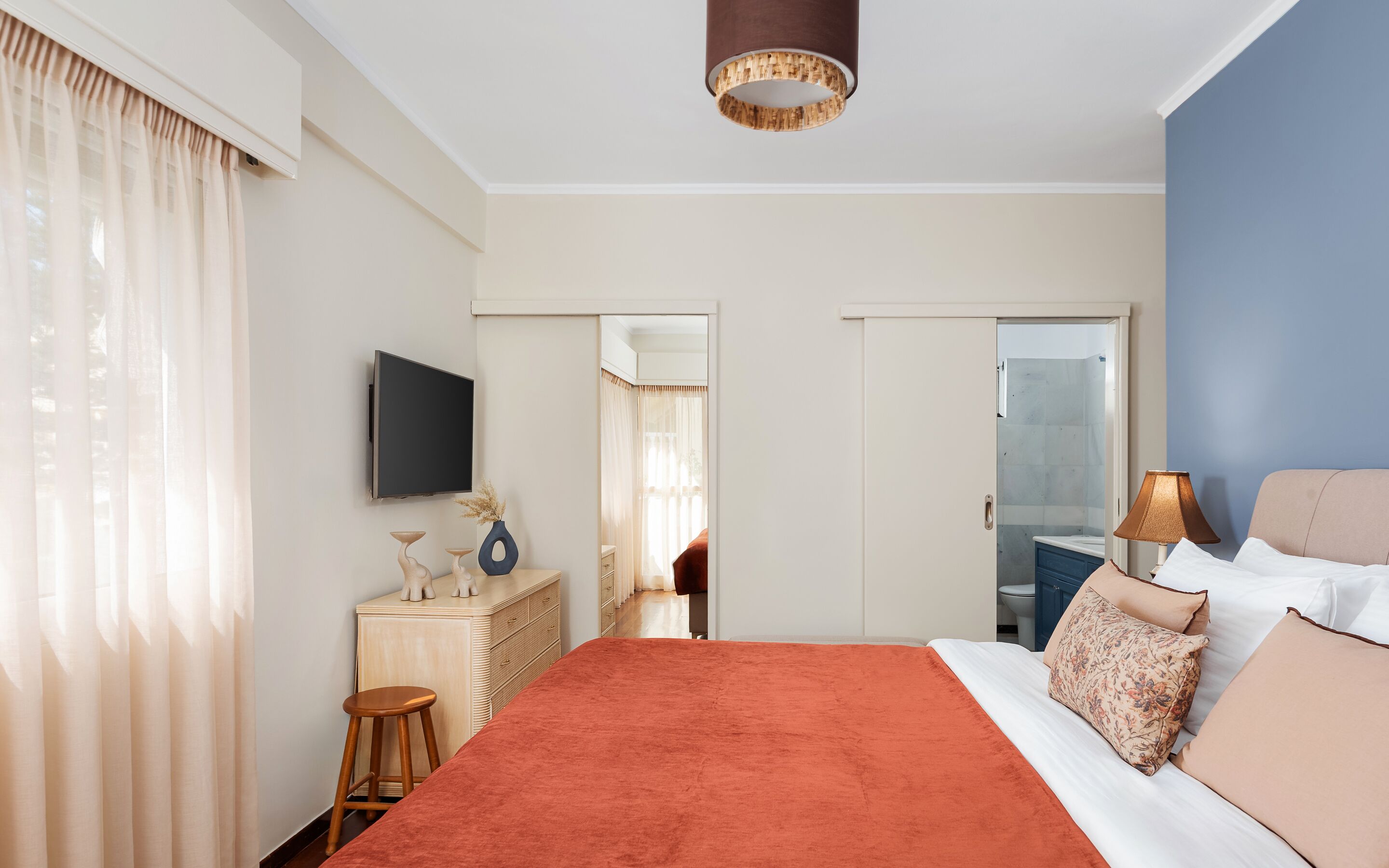 A hotel room with a bed, a TV, a desk, a mirror, and a bathroom visible through an open door.
