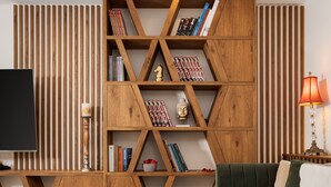 A modern living room with a wooden bookshelf, a green sofa, a glass coffee table, and a television. - Voula Calm Living (Voula)