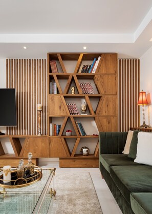 Ein modernes Wohnzimmer mit einem Holzregal, einem grünen Sofa, einem Glastisch und einem Fernseher.