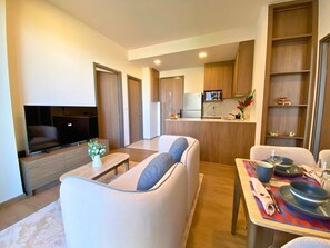 Ein modernes Wohnzimmer mit Flachbildfernseher, einer Couch, einem Couchtisch und einem Essbereich mit Tisch für zwei Personen.